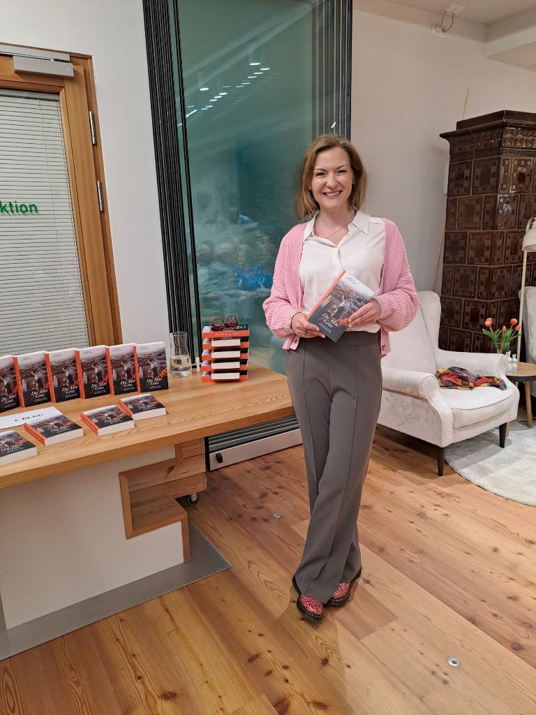 Foto von der Autorin - sie steht zirka in der Mitte des Bildes vor einem Tisch mit Exemplaren ihres Buches